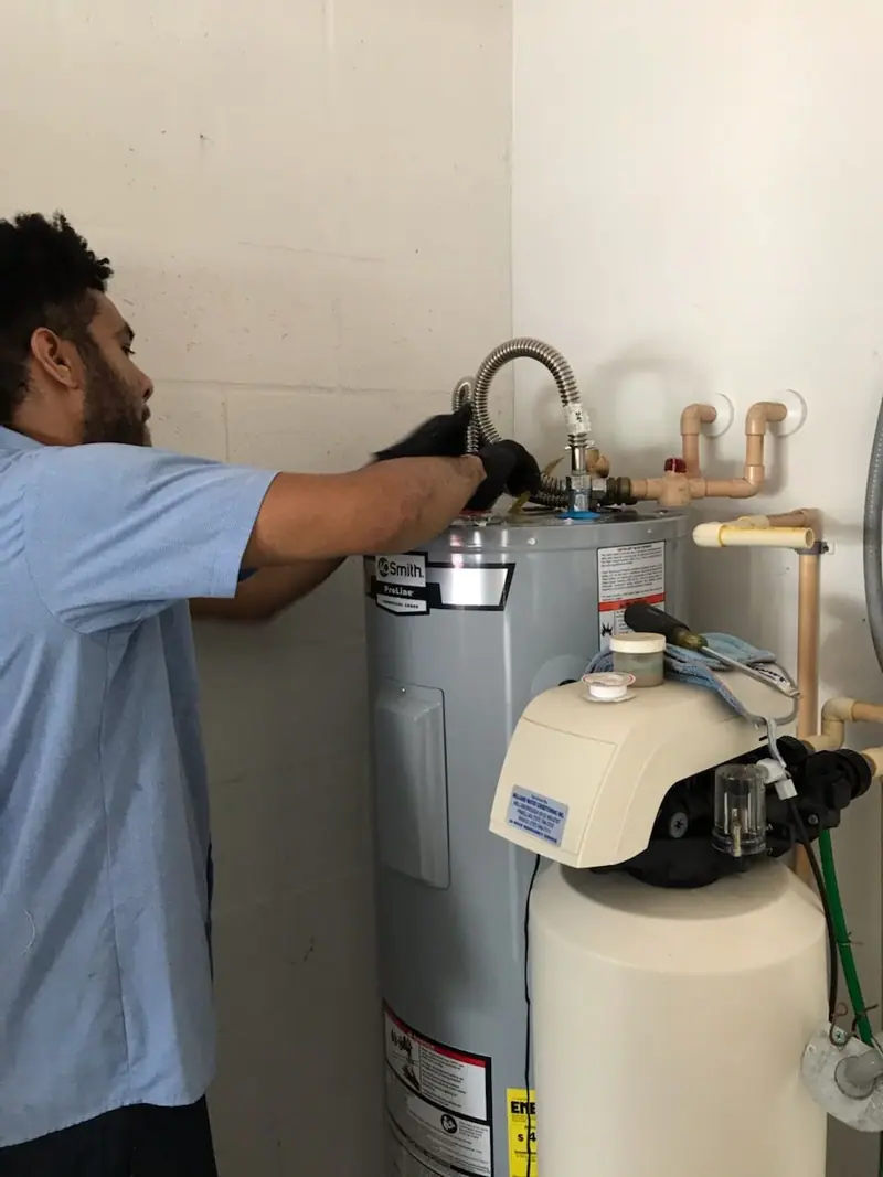 3 J's plumber connecting supply lines on a water heater beside a whole house softener